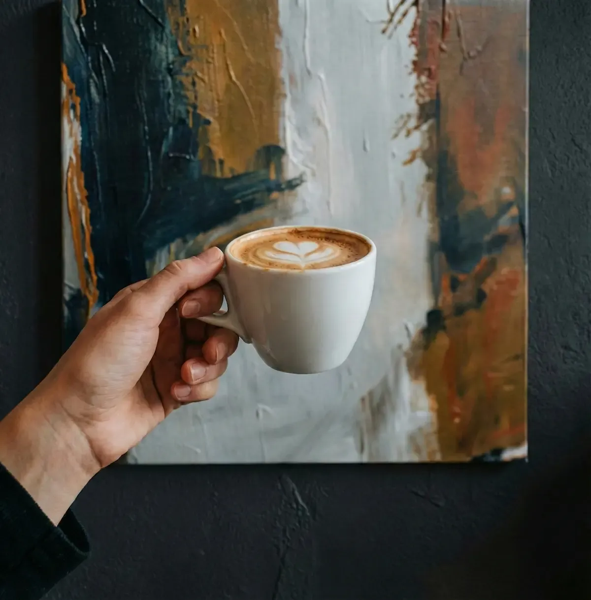 Tasse de cappuccino tenue devant une toile abstraite du Sdakox